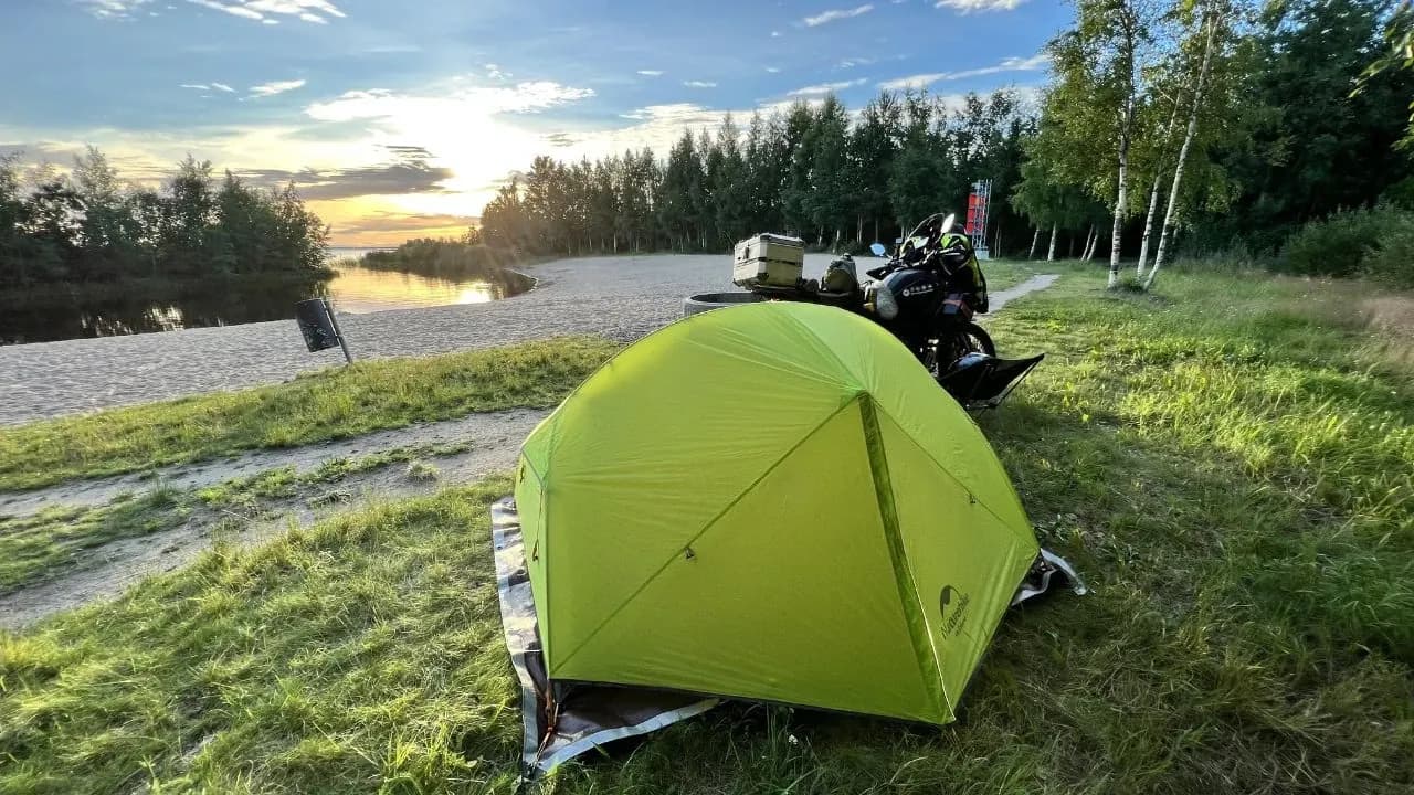 Tienda de campaña y moto de aventura acampando libremente junto a un lago nórdico al atardecer