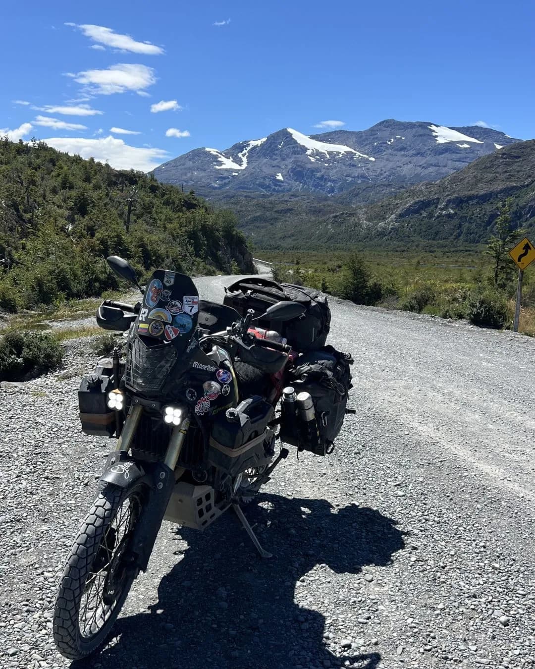 Loaded motorcycle on dry gravel facing snowy mountains